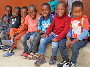 Kindergartenkinder der Gemeinde Welverdiend in Südafrika sitzen nebeneinander auf einer Bordsteinkante