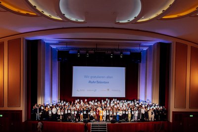 200 Schülerinnen und Schüler stehen auf einer Bühne und halten ihre Stipendien in die Höhe