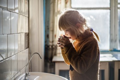 Ein Kind trinkt ein Glas Wasser vor einem Waschbecken