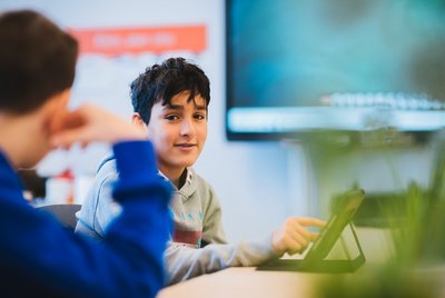 Ein Kind sitzt im Klassenraum und bedient ein Tablet im Rahmen der digitalen Unterstützungsangebote