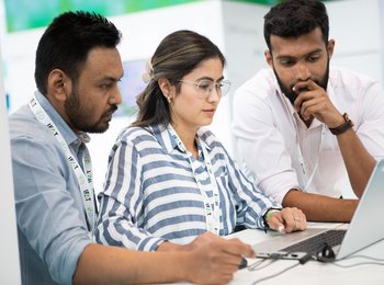 Studierende stehen konzentriert vor einem Laptop