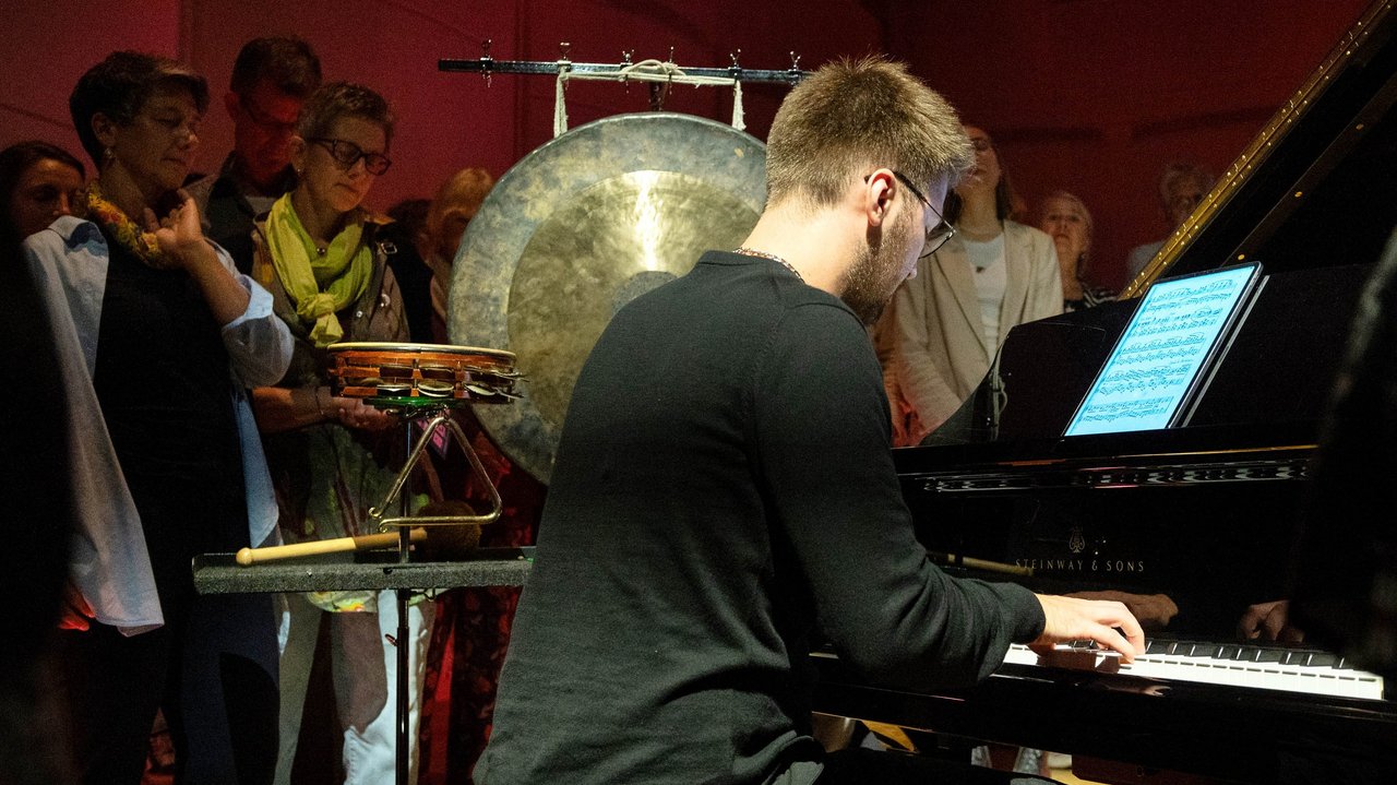 Ein Musiker sitzt an einem Klavier, umgeben von Zuschauenden