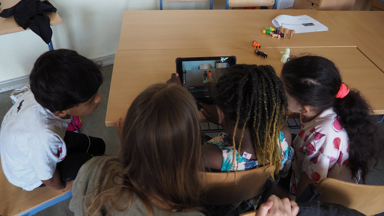 Kinder im Klassenraum sitzen interessiert vor einem Tablet